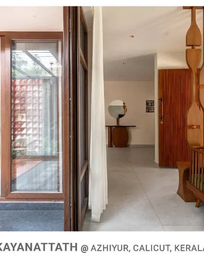 A look from the living space towards the entrance at Kayanattath House, where the open layout and wooden screen partition maintain a visual connection to the courtyard and other areas.