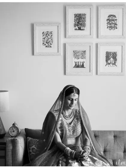 A pensive black and white portrait of a bride sitting on a couch. The quiet moment of reflection before the ceremony is captured with artistic elegance.
