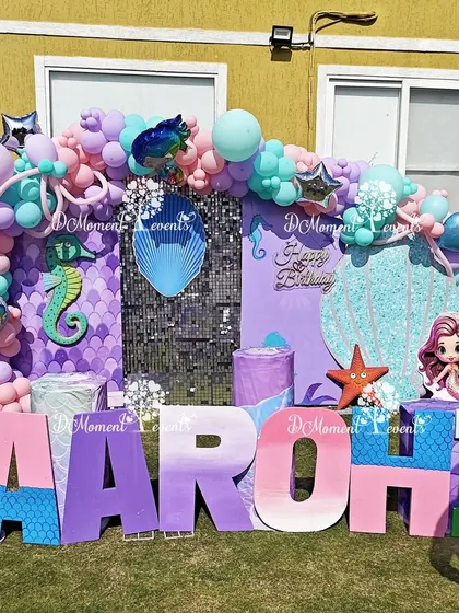 A close-up of the vibrant outdoor mermaid stage, showing the detailed props like the seahorse, starfish, and the custom-painted marquee letters.