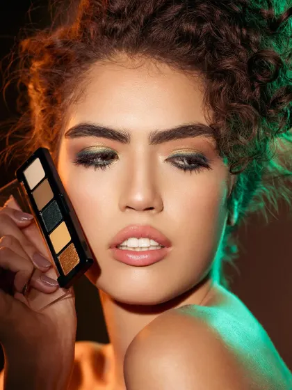 This image showcases a complete eyeshadow look, with the model holding the palette that created it. The lighting is carefully crafted to highlight both the makeup on her eyes and the product itself, creating a direct link between the tool and the beautiful result.