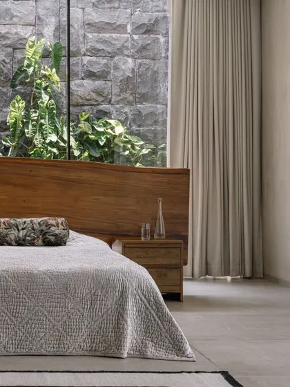 A closer look at the master bed, with its custom live-edge headboard and the view of the stone-clad courtyard wall. This composition perfectly illustrates our modern organic design philosophy.