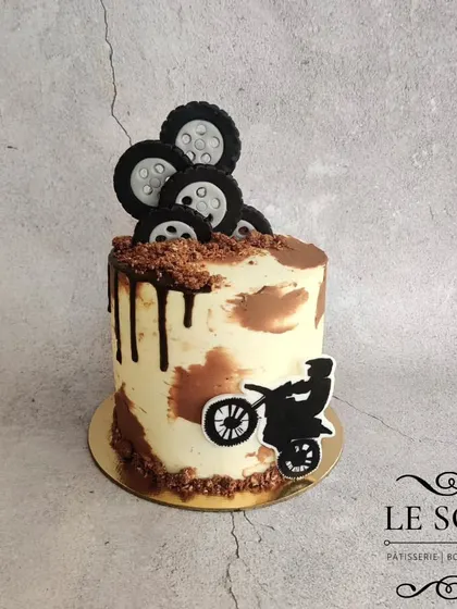 A rugged dirt bike theme for an enthusiast. This 1 kg Ferrero Crunch cake features a camouflage buttercream effect, a dark chocolate drip, cocoa crumble "dirt," and fondant tires.