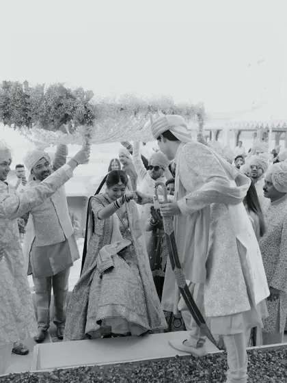 A timeless black and white photograph of a traditional wedding ritual. The groom helps the bride during the ceremony, a moment of partnership and tradition captured beautifully.