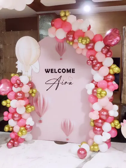 A sweet "Welcome Home" decoration for a baby girl. This setup features a pink balloon arch with hot air balloon accents and a cute baby character cutout, creating a lovely backdrop for photos.