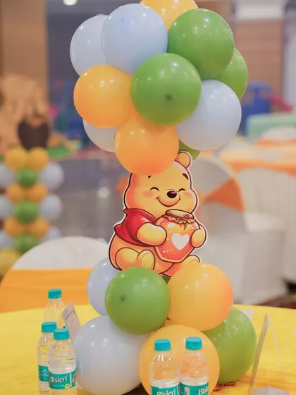 A close up of a Winnie the Pooh table centerpiece, with a character cutout attached to a balloon cluster in theme colors.