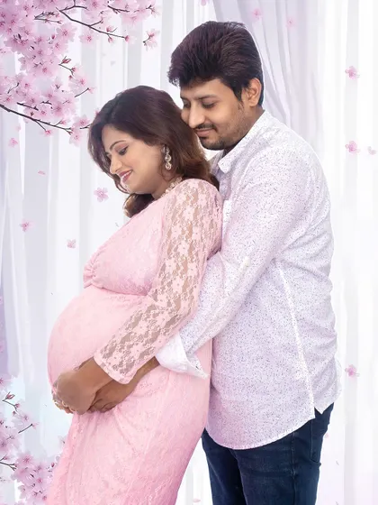A gentle and romantic pose with the couple surrounded by a soft, dreamy floral background. The mom-to-be's pink lace dress adds to the delicate feel of the portrait.