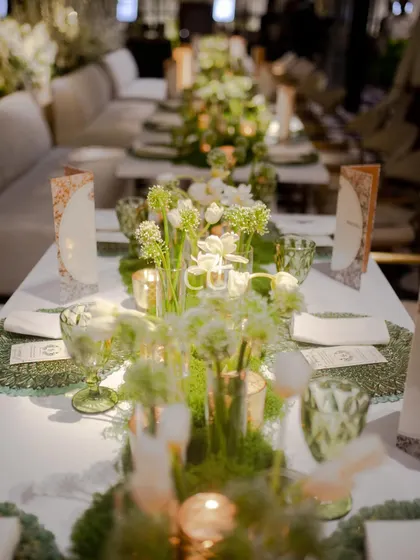 An example of our integrated approach to decor and dining. This elegant table setting features a lush moss runner, delicate white florals, and custom menus, creating a cohesive and enchanting garden-themed dining experience for guests.