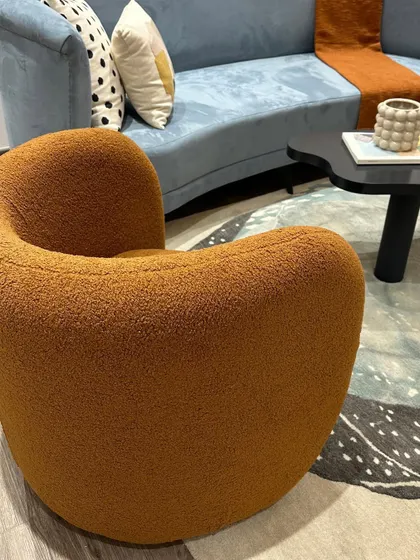 A close-up of our 'Otto' accent chair, upholstered in a cozy, textured orange boucle fabric. Its curved form is both modern and inviting.