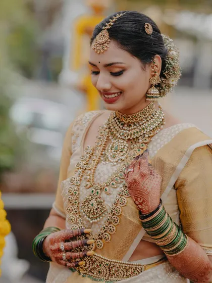 A picture of pure grace. This bride's look is a testament to classic elegance, with her golden Kanjeevaram saree, layered temple jewellery, and a makeup look that is both radiant and understated, letting her natural happiness shine through.