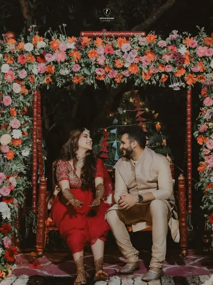 A beautiful shot of the couple during their Mehendi ceremony, sharing a quiet moment under a stunning floral arch.