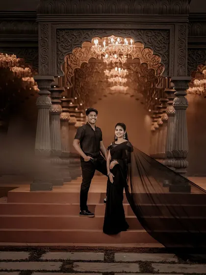 The couple stands on the steps of a grand venue, illuminated by chandeliers, creating a moody and romantic pre-wedding photograph.