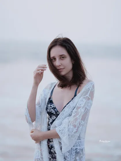 A candid moment captured on the beach, with the wind gently blowing the model's hair. It feels natural and unstaged.