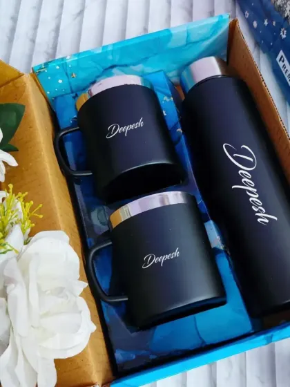 A sleek and modern personalized drinkware set. This gift box includes a matte black temperature bottle and two matching stainless steel mugs, all customized with the name "Deepesh" in an elegant script.