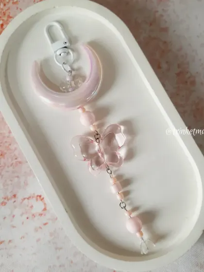 A product shot of my pink moon and butterfly charm on a clean, white tray, highlighting its delicate details and blush tones.