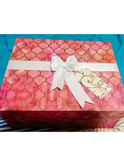 The exterior of a beautifully patterned pink gift box, tied with a white ribbon and a birthday tag.