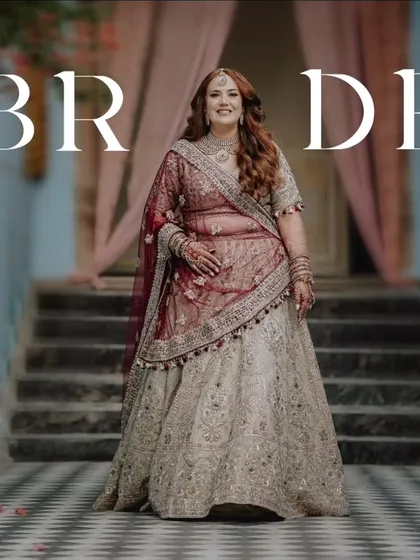 A full-length portrait of the bride, her hands gracefully posed, showcasing her magnificent wedding lehenga and regal bearing.