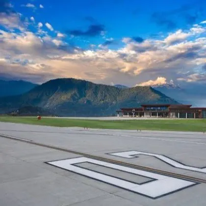 A ground-level view from the runway, looking towards the terminal with the Himalayas in the background. This perspective captures the feeling of arrival and the successful integration of a major infrastructure project into a breathtaking natural setting.