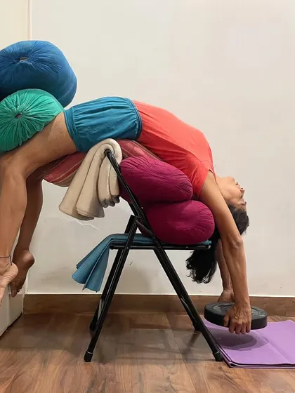 This is an advanced supported backbend using a chair, bolsters, and weights. This complex setup provides deep opening for the spine and chest while ensuring the body is held safely, allowing for a profound therapeutic effect.