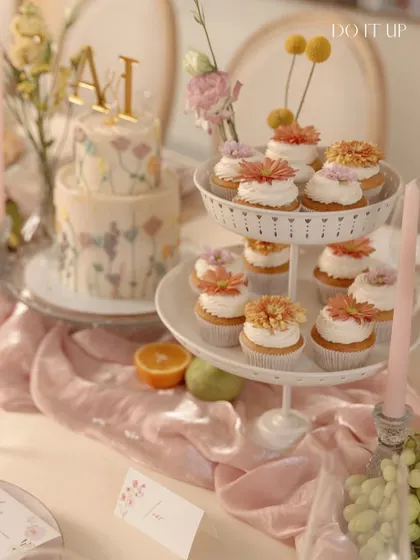 A dessert table from a floral-themed anniversary brunch. A two-tiered cake with hand-painted wildflowers and matching cupcakes are beautifully displayed, adding a sweet and artistic touch to the celebration.
