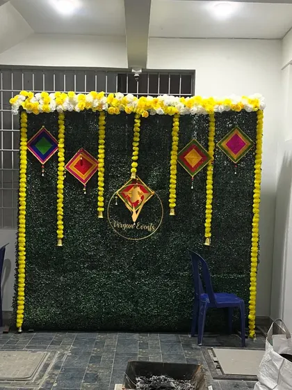 A simple yet festive backdrop for a Haldi or Mehendi ceremony, using a green hedge wall and marigold garlands.
