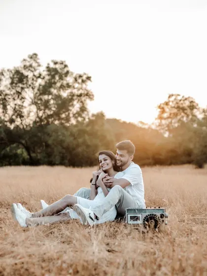 A romantic sunset shot of a couple relaxing in a field with a retro boombox, creating a nostalgic and warm atmosphere.