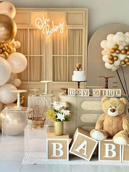A full teddy bear themed baby shower setup. This design uses a neutral palette with gold and white balloons, "BABY" blocks, and multiple dessert stands for a complete look.