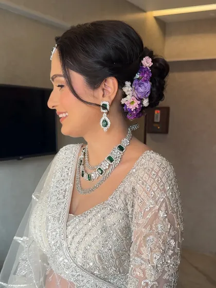 A side profile showing the beautiful floral bun with purple and pink flowers. This adds a lovely, soft touch of color to her elegant ivory reception look.
