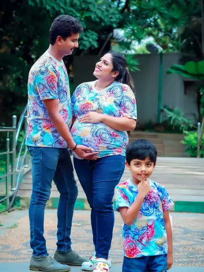 A happy family portrait in a park, with everyone in colorful matching t-shirts, celebrating the upcoming arrival.