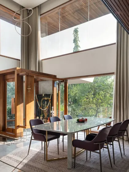 The same double-height space, transformed into a light-filled dining area with a modern puja room. The design connects two levels and opens to the outdoors, creating a sense of volume and serenity.