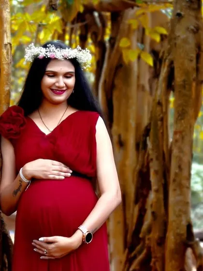 A serene portrait of a mom-to-be in a red gown, set against the beautiful texture of banyan tree trunks. The floral crown adds a soft, natural touch.