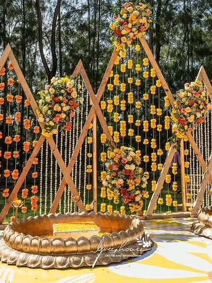 A modern Haldi setup with a geometric backdrop of hanging marigold strings.