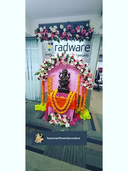 A close-up of the Ganpati idol setup in the office, framed by a beautiful arch of pink, red, and white flowers. We pay close attention to the details to create a respectful and beautiful display.