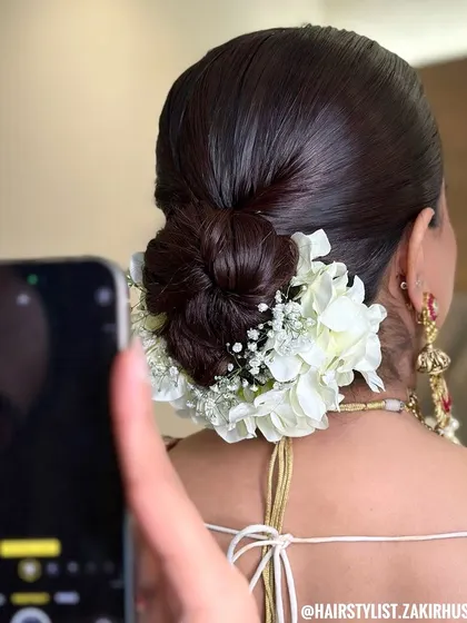 A clean and classic bridal juda, wrapped in a garland of fresh white hydrangeas and baby's breath. This is a timeless choice that photographs beautifully and keeps the focus on the bride's features.
