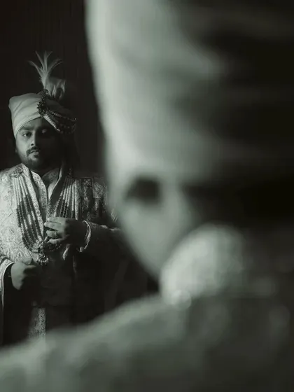 A creative shot of the groom looking at his reflection, a moment of introspection before the wedding ceremony.