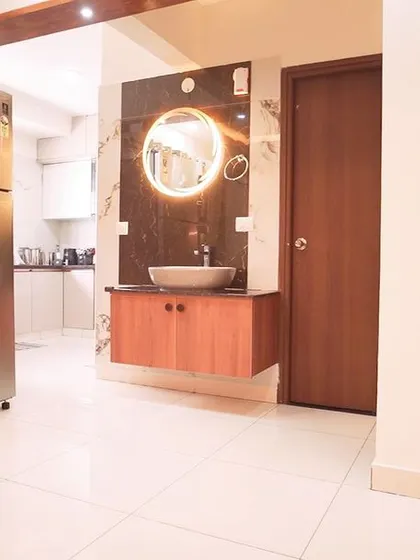 A view from the dining area towards the kitchen, showing a stainless steel refrigerator and a modern vanity unit with a backlit mirror. This highlights the flow between different functional zones.
