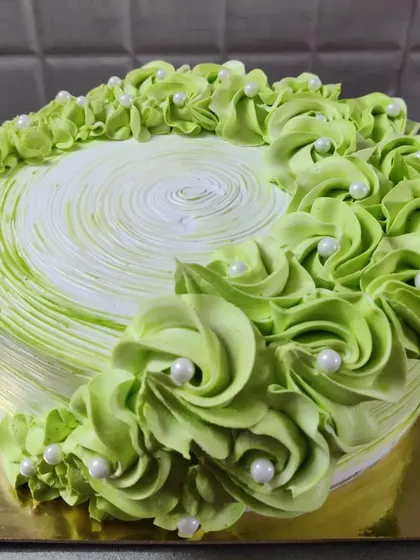A lovely green cake with piped rosettes and white pearls. The swirl pattern on top adds a nice finishing touch.
