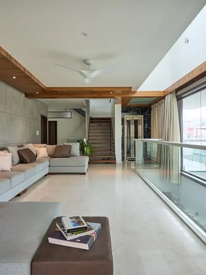 The family lounge in 'Wilasa' features a concrete-paneled accent wall and a large sectional sofa. The full-length glass balcony offers expansive views and fills the room with natural light.