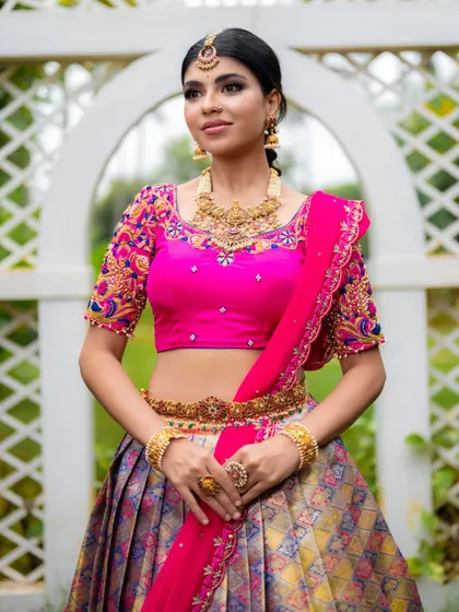 A close-up of the pink blouse, showcasing the intricate hand embroidery and the traditional jewelry it's paired with.