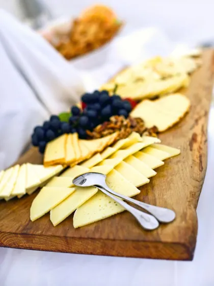 A rustic wooden board laden with a variety of cheeses, grapes, and walnuts. This makes for a perfect savory dessert course or a sophisticated addition to a wine and cheese event.