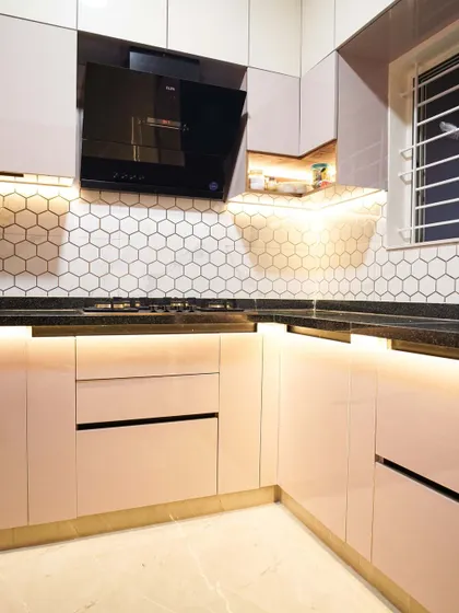 This L-shaped kitchen features a modern hexagonal tile backsplash in white, creating a clean and contemporary look. The warm under-cabinet and toe-kick lighting adds a cozy and luxurious feel to the space.