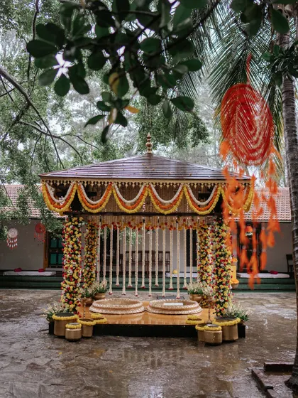The Haldi mandap stands beautifully in the rain-soaked courtyard, its vibrant yellow and orange colors creating a stunning contrast with the wet stone and lush greenery.