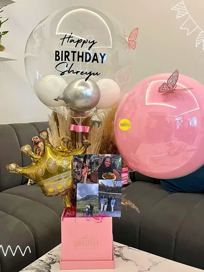 A sweet and personal birthday bouquet in a pink box, complete with a custom bubble balloon, photos, and butterfly details.