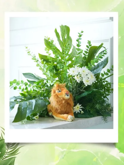 A close-up of a centerpiece featuring a plush lion surrounded by lush greenery, showcasing the detailed and thoughtful styling of the jungle theme.