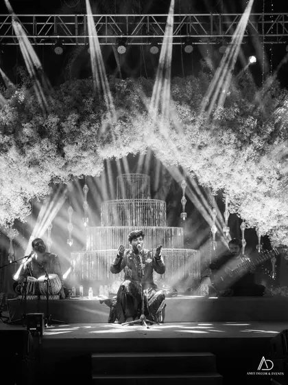 A black and white shot of a live band performing on the sangeet stage, with dramatic spotlights cutting through the haze, creating a powerful and atmospheric scene.