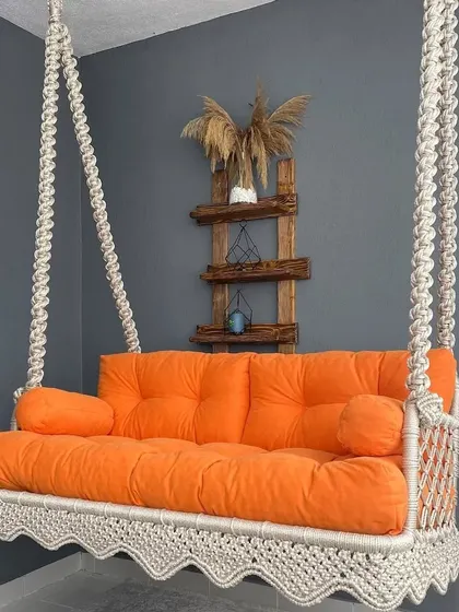 Our macrame sofa swing with a bright orange cushion. This piece adds a pop of color and a lot of comfort to any room, perfect for lounging with family and friends.