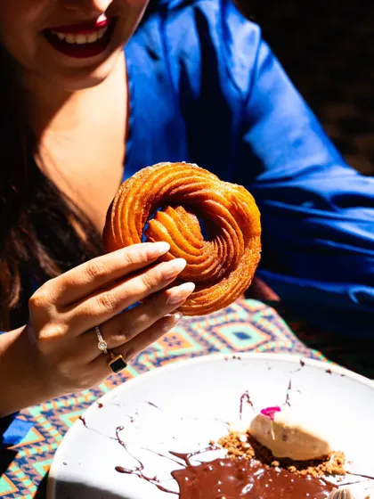 A close-up on a churro dessert at Lyla Bombay. The focus on the person's smile and the delicious-looking treat creates a feeling of joy and indulgence.