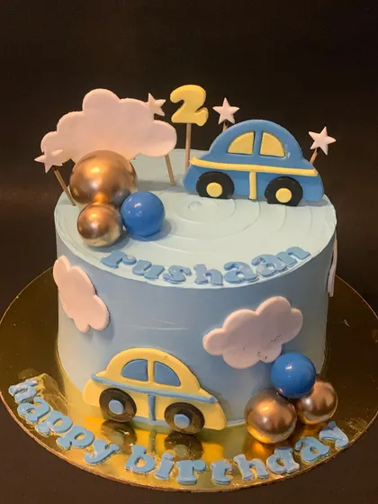 A dreamy car themed cake with fondant clouds and stars. The blue cake is decorated with cars and metallic chocolate spheres.