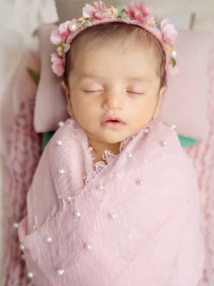 Pretty in pink! This close-up shows a newborn swaddled in a pearl-adorned pink wrap, complete with a matching floral headband.