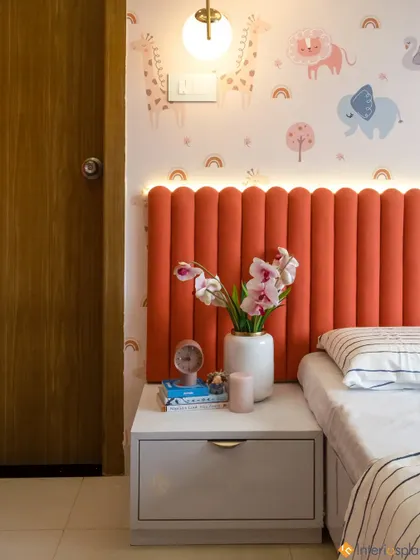 A close-up of the bedside area in a child's room, featuring a vibrant orange fluted headboard and a cute animal-themed wallpaper.