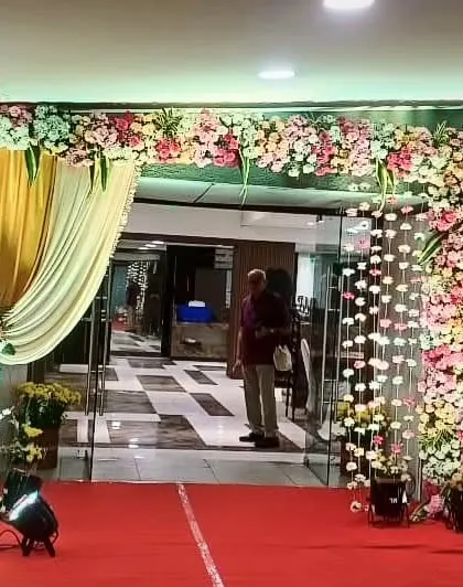 A beautiful floral entrance for an indoor event. The arch is made of pastel pink and white flowers, with hanging floral strings on one side for an added touch of elegance.